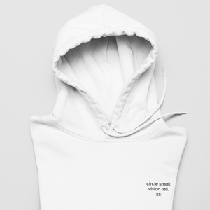 White hoodie pullover reading "circle small vision tall" on a grey surface